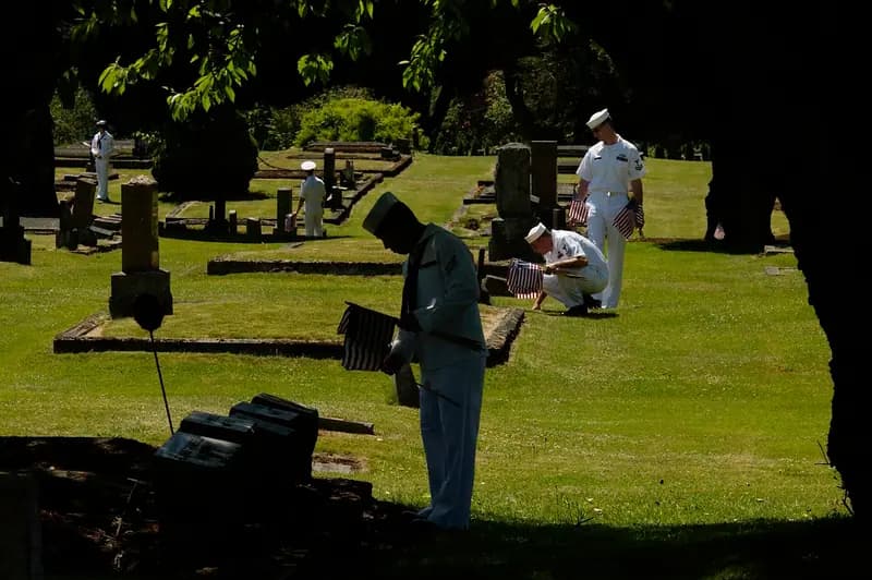 Sailors from Naval Station Everett place flags at veterans' headstones under the shade of old trees