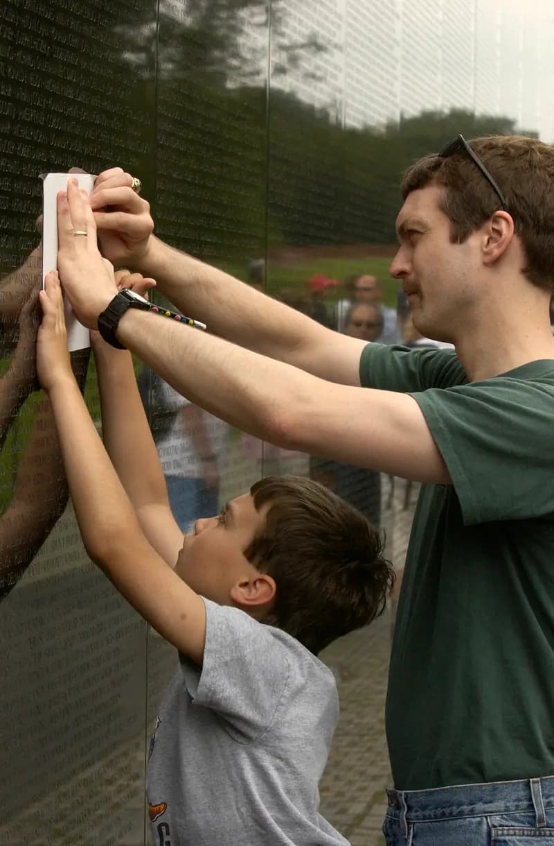 A father helps his son make a rubbing of a great uncle's name on the Vietnam Veterans Memorial