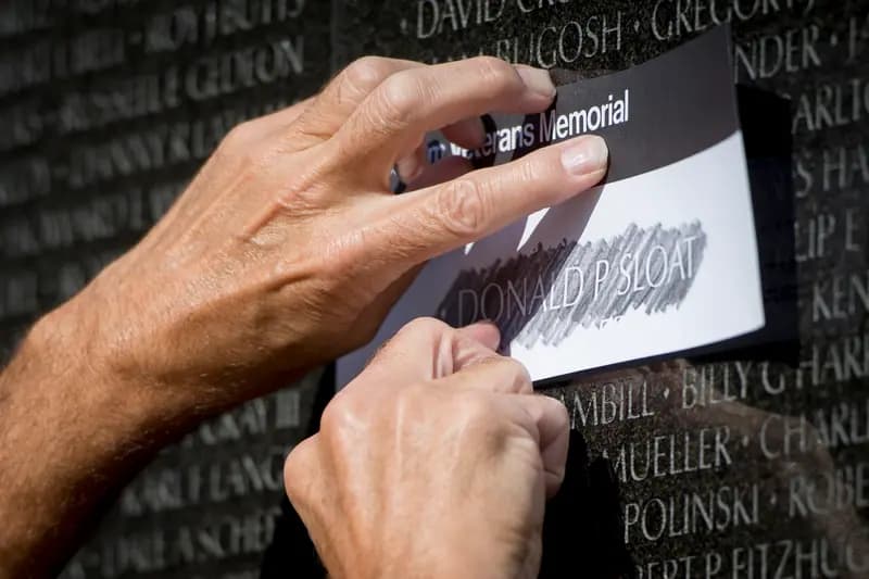Hands make a pencil rubbing of a name engraved on the Vietnam Veterans Memorial